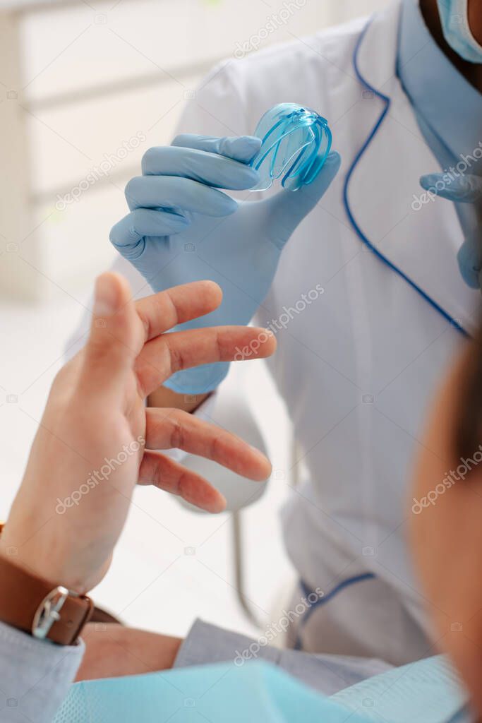 cropped view of dentist in latex gloves pointing with finger at retainer near patient 