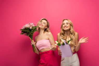 Pozitif sarışın kızlar pembe arka planda çiçek buketleri tutuyorlar.