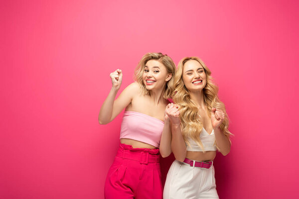 Smiling blonde women showing yeah gesture on pink background