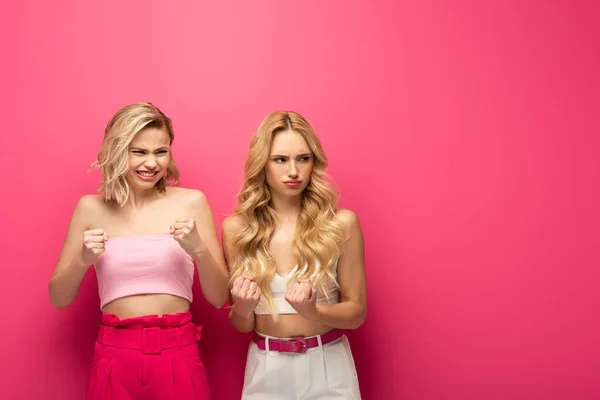 Angry blonde women with fists looking away on pink background