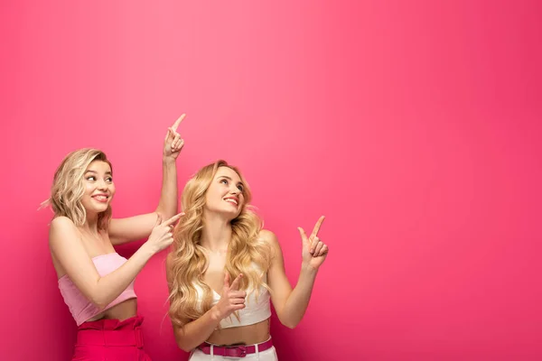 Щасливі Блондинки Вказують Пальцями Дивляться Вгору Рожевий Фон — стокове фото