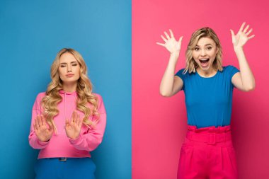 Blonde woman showing stop sign near excited sister on pink and blue background