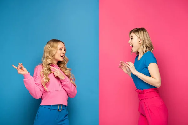 Smilende Blond Kvinne Med Fingrene Mot Sjokkert Søster Rosa Blå – stockfoto