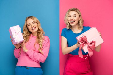 Mavi ve pembe arka planda fiyonklu hediye kutuları tutan mutlu sarışın kadınlar.