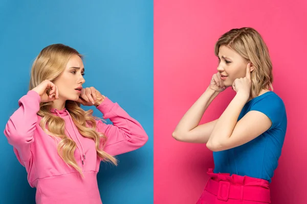 Скептичні Сестри Блондинки Прикривають Вуха Дивлячись Один Одного Рожево Блакитному — стокове фото