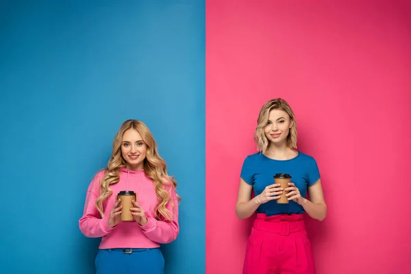 Smiling Blonde Sisters Holding Paper Cups Pink Blue Background — Stock Photo, Image