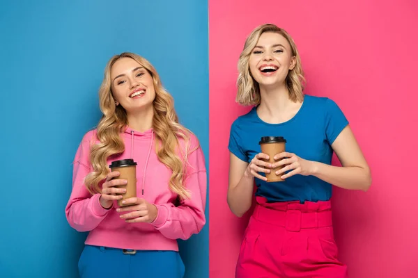 Positive Blonde Sisters Paper Cups Smiling Camera Pink Blue Background — Stock Photo, Image