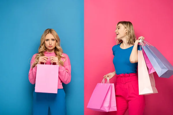 Smiling Girl Shopping Bags Looking Offended Sister Pink Blue Background — Stock Photo, Image