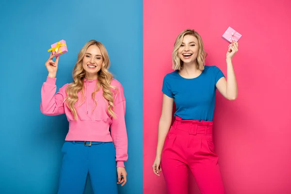 Smiling Blonde Girls Holding Presents Looking Camera Blue Pink Background — Stock Photo, Image