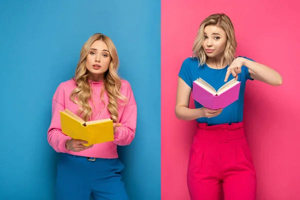 Hermanas Rubias Confundidas Mirando Cámara Mientras Sostienen Libros Sobre Fondo —  Fotos de Stock