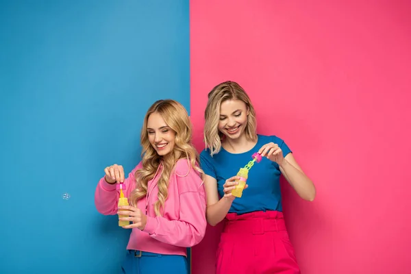 Smiling Blonde Sisters Soap Bubbles Pink Blue Background — Stock Photo, Image