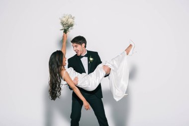 Heyecanlı damat beyaz arka planda mutlu Afro-Amerikan gelinini tutuyor.