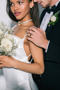 Güzel Afrikalı Amerikalı gelinin omzuna dokunan damat manzarası beyaz arka planda düğün buketi tutuyor.