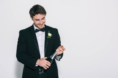 Mutlu damat beyaz arka planda şampanya şişesi açıyor.