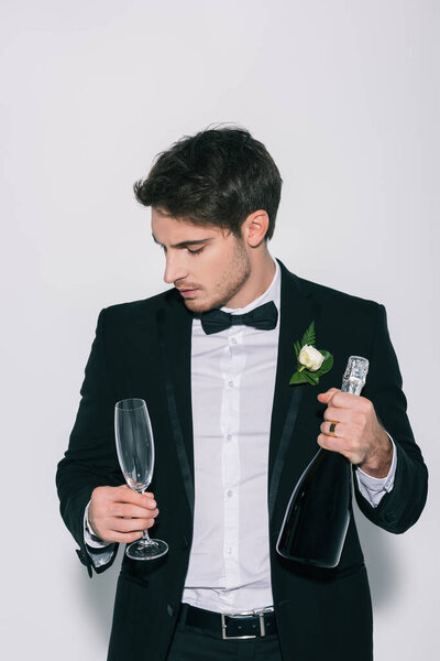 pensive bridegroom holding champagne glass and bottle on white background
