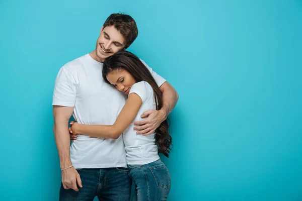 Feliz Casal Interracial Abraçando Com Olhos Fechados Fundo Azul — Fotografia de Stock