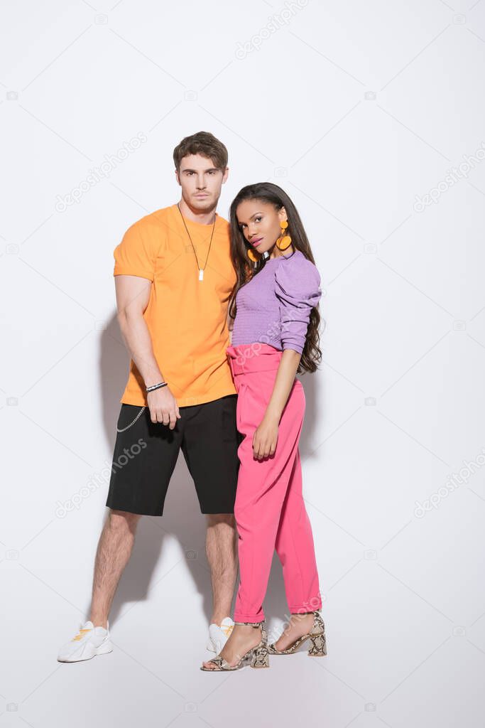 full length view of stylish african american girl and handsome young man looking at camera on white background