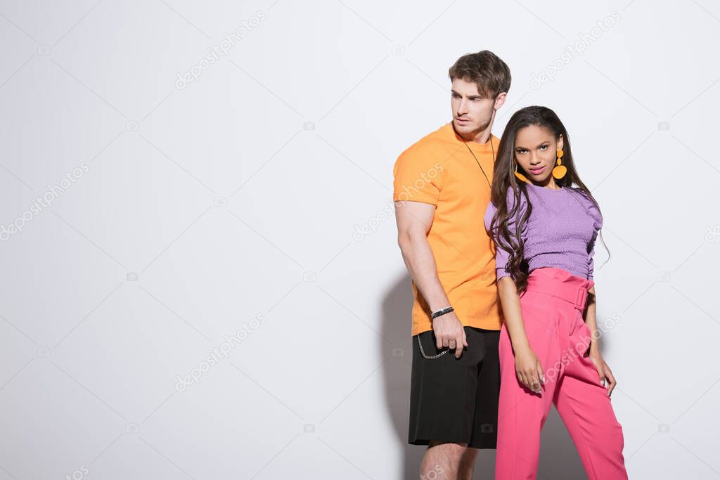 fashionable african american girl looking at camera near handsome boyfriend looking away on white background