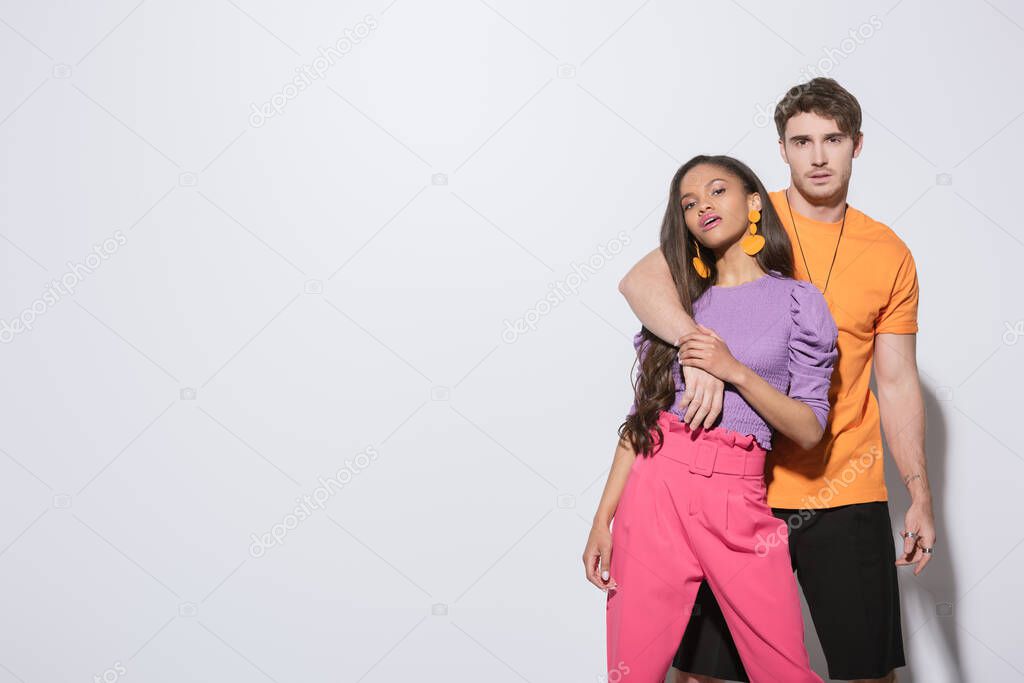 handsome guy embracing trendy african american girlfriend while looking at camera on white background