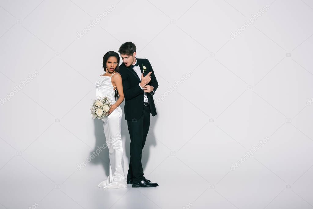 full length view of elegant interracial newlyweds standing back to back on white background