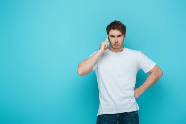Hoşnutsuz adam mavi arka planda akıllı telefonla konuşurken kalçasını tutuyordu.