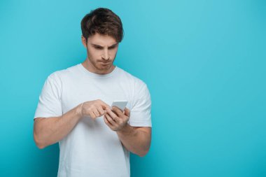 Mavi arka planda akıllı telefon kullanan konsantre genç adam