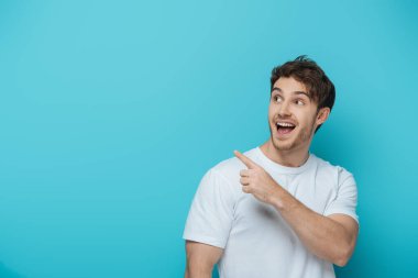 surprised guy looking away and pointing with finger on blue background clipart