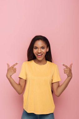 smiling african american girl pointing with fingers at braces on her teeth on pink background clipart