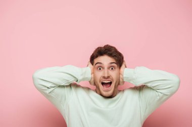 scared man screaming while covering ears with hands on pink background clipart