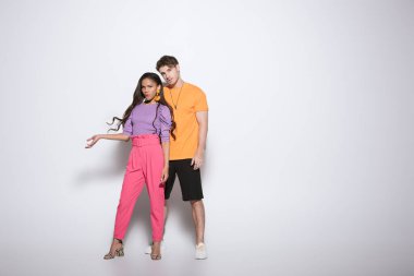 Beyaz arka planda yakışıklı erkek arkadaşının yanında kollarını açmış modaya uygun Afro-Amerikan kız manzarası.