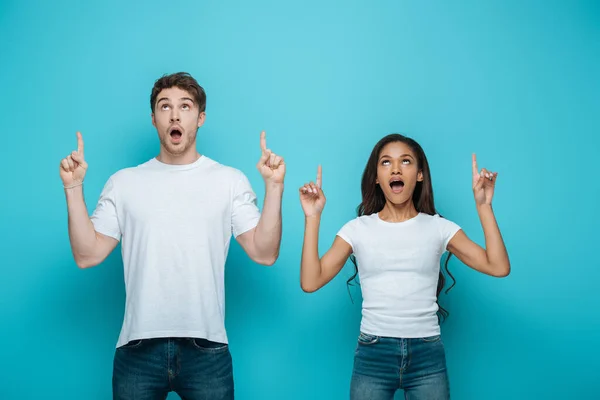 Chocado Interracial Casal Olhando Para Cima Apontando Com Dedos Azul — Fotografia de Stock