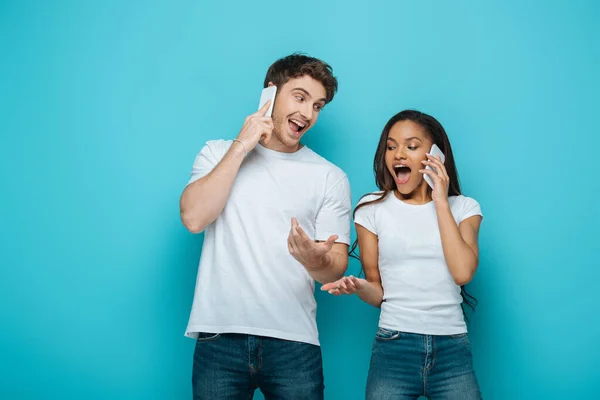 Animado Interracial Casal Com Braços Abertos Falar Fundo Azul — Fotografia de Stock