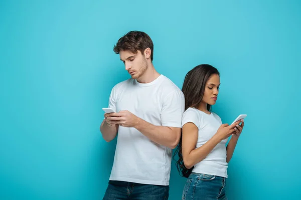 Young Interracial Couple Chatting Smartphones While Standing Back Back Blue — Stock Photo, Image