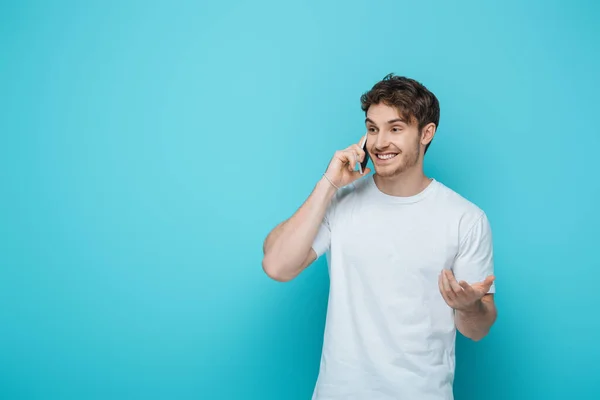 Cara Alegre Com Braço Aberto Enquanto Fala Smartphone Fundo Azul — Fotografia de Stock