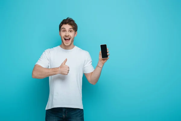 Heyecanlı Genç Adam Mavi Arka Planda Boş Ekranlı Akıllı Telefonu — Stok fotoğraf
