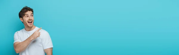 Горизонтальное Изображение Удивленного Парня Смотрящего Сторону Указывающего Пальцем Синий Фон — стоковое фото