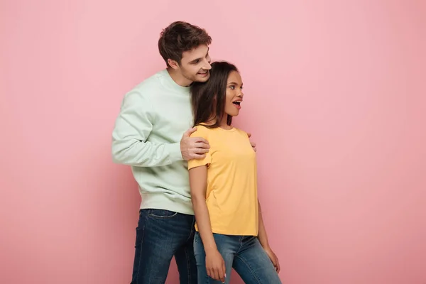 Smiling Man Touching Shoulders Amazed Girlfriend Looking Away Pink Background — Stock Photo, Image