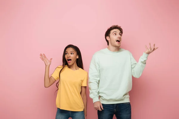 Shocked Interracial Couple Standing Open Arms While Looking Away Pink — Stock Photo, Image