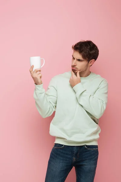 Thoughtful Guy Touching Chin While Looking White Cup Pink Background — Stock Photo, Image