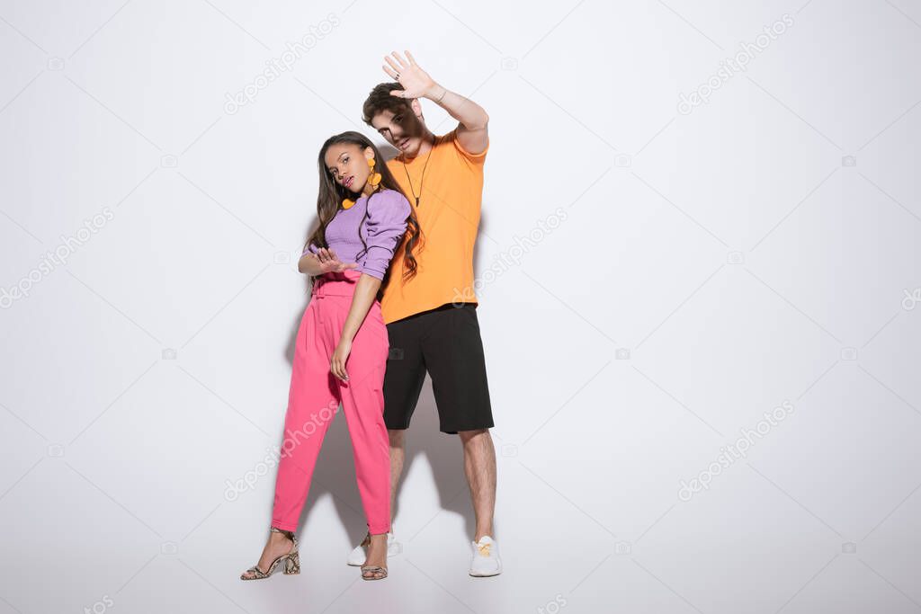 full length view of stylish african american girl looking at camera near handsome boyfriend standing with outstretched hand on white background