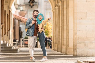 Sokakta sarılan ve parmağıyla işaret eden resimli yüzleri olan iki turist.
