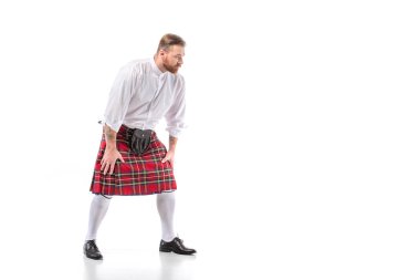Scottish redhead man in red kilt in pose on white background clipart