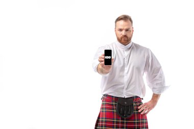 KYIV, UKRAINE - Kasım 29, 2019: kırmızı kiltli ciddi İskoç kızıl saçlı adam HBO uygulamalı akıllı telefonu beyaza aktarıyor.