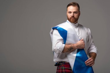 İskoçya bayrağı gri arka planda kırmızı etekli ciddi İskoç kızıl saçlı adam.