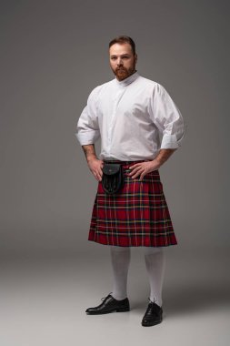 Scottish redhead man in red kilt on grey background clipart