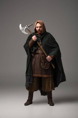 Şömine rafında gri arka planda savaş baltası olan İskoç kızıl saçlı bir adam.