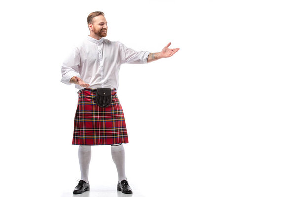 smiling Scottish redhead man in red kilt gesturing on white background
