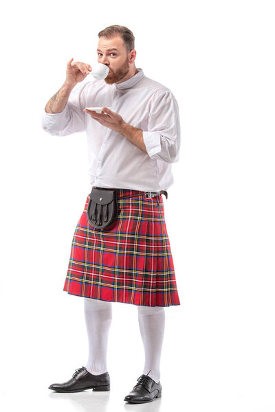 Scottish redhead man in red kilt drinking coffee on white background