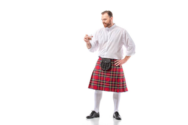 Scottish redhead man in red kilt with whiskey in glass on white background