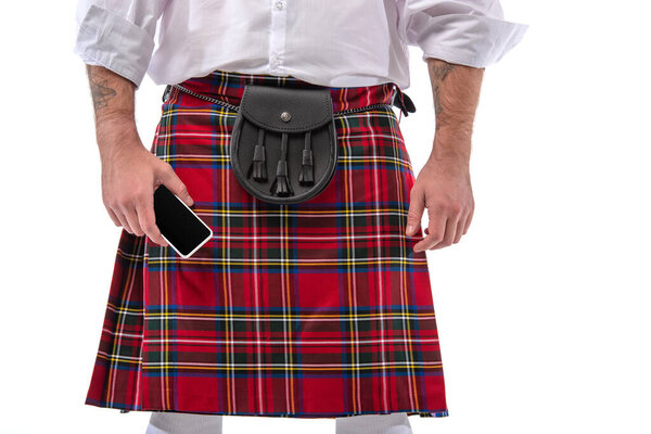 cropped view of Scottish man in red kilt with leather belt bag and smartphone isolated on white